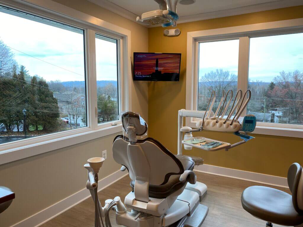 Modern dental exam room with a patient chair, dental equipment, and large windows overlooking a scenic landscape.